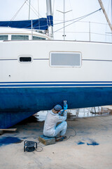 a man polishing the side of the hull of a blue ship.