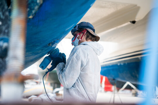 a man polishing the side of the hull of a blue ship.