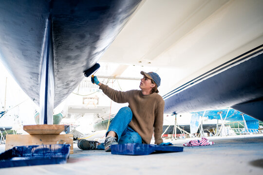 A man painting the hull of a ship with blue paint.