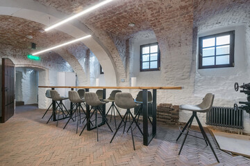 Modern industrial workspace with stylish seating and bright lighting in a renovated historic building. A spacious room features a long wooden table with modern chairs, exposed brick walls