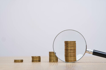 Close-up of stacked coins on a table with a magnifying glass, symbolizing financial growth and...
