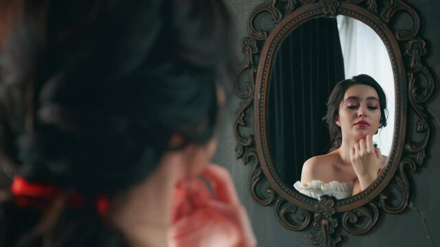 Fantasy princess woman looks at herself reflection in vintage old style antique mirror touching beauty face with hand. Elegant hairstyle natural makeup eyes lips. Girl Fashion model posing. Dark room