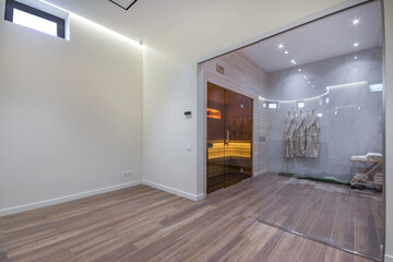 A modern home interior featuring a sauna with glass doors and wooden floors. A small table with towels and bathrobes on hooks.