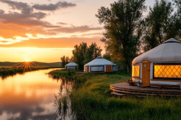 A line of yurts stretching along a riverbank, with reflections shimmering in the water and trees swaying in the breeze