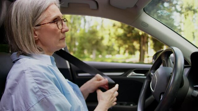 Serious Caucasian elderly female business woman mature businesswoman aged car driver rental service client open auto door sitting inside automobile fastens seat belt safe driving leaving ride vehicle