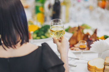 Human hands with glasses of alcohol clinking them over served table. People at the table at a solemn event clink glasses and celebrate. A glass in a hand closeup