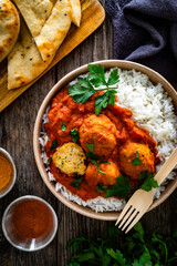 Butter chicken curry meatballs with rice in box to go on wooden table. Takeaway indian food