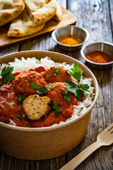 Butter chicken curry meatballs with rice in box to go on wooden table. Takeaway indian food
