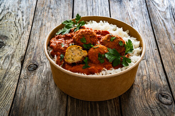Butter chicken curry meatballs with rice in box to go on wooden table. Takeaway indian food