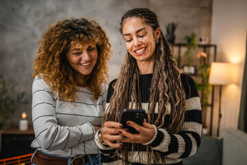 two female friends use mobile phone and have fun together at home