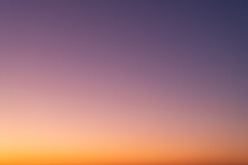 Clear sunset sky background. Vibrant gradient from orange to purple. Beautiful and natural color transient without any clouds. Real sky view.