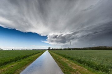 Dramatic contrast between clear blue sky and dark storm clouds over a rural road in a tranquil landscape
