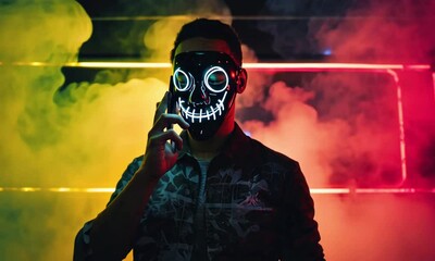man in a scary glowing death mask holds a phone to head, smokes and nods in a neon flashing light with glitch effect - Powered by Adobe