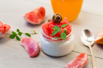 homemade sweet yogurt in a glass jar with pieces of red ripe grapefruit and honey, on a wooden table