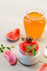homemade sweet yogurt in a glass jar with pieces of red ripe grapefruit and honey, on a wooden table