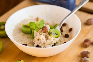 cooked oatmeal with kiwi, honey and nuts in a bowl on a wooden table