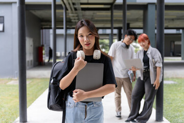 Portrait of a smiling asian female student holding a laptop with her classmates collaborating on a project in the background at university campus