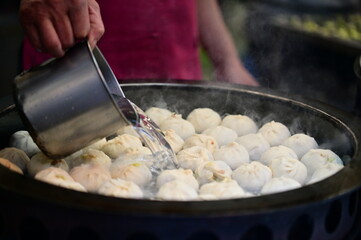 A street vendor skillfully pours water into a frying pan filled with shuijianbao. This essential step ensures the buns are both crispy and tender, creating the perfect texture.