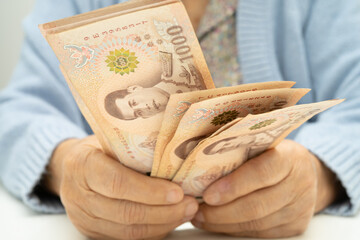 Obraz premium Asian elder senior woman patient holding Thai banknotes money in her hand, Cost of living and medical care.