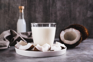 Fresh coconut milk in a glass and coconut pieces on a plate on the table
