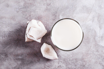 Close up of fresh coconut milk in a glass and coconut pieces on a plate on the table top view