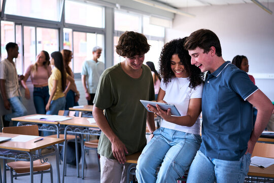 A group of multiracial students gather around a digital tablet in the classroom during a break, sharing a moment of curiosity and connection in a friendly and inclusive learning environment