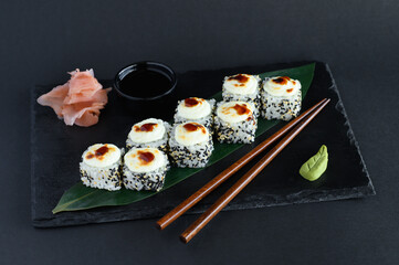 A set of sushi rolls on a wooden board and banana leaf, served with soy sauce, wasabi, ginger, and chopsticks. Perfect for an Asian restaurant menu.