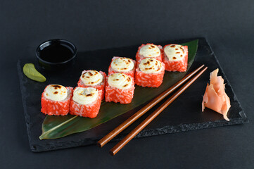 A set of sushi rolls on a wooden board and banana leaf, served with soy sauce, wasabi, ginger, and chopsticks. Perfect for an Asian restaurant menu.