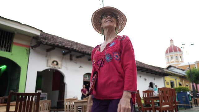 A mature woman enjoys her trip in Granada, Nicaragua, wearing a colorful outfit and a sun hat while strolling through the lively streets filled with charm.