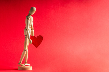 Wooden model of a man holds a wooden figure of a heart in his hands on a red background. Mockup of...