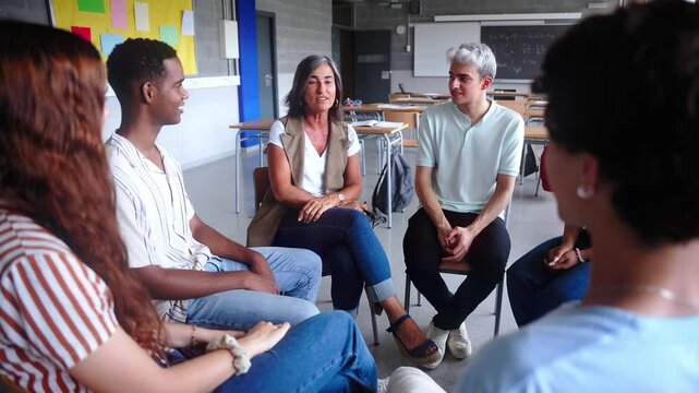Diverse group of high school students sitting on chairs in a circle and interacting during a lesson, their Caucasian male teacher with them and talking. Education concept. High quality photo