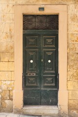 An old door dark green to a flat in the alleyways of Maltas historic old towns.