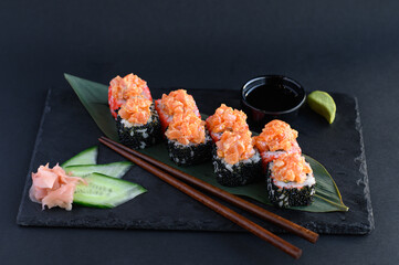 A set of sushi rolls on a wooden board and banana leaf, served with soy sauce, wasabi, ginger, and chopsticks. Perfect for an Asian restaurant menu.