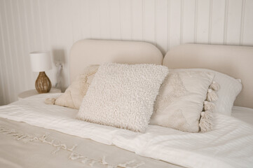 Beautiful light beige interior with soft white bed decorated with pillows in japandi and wawabi sabi style, cozy home concept