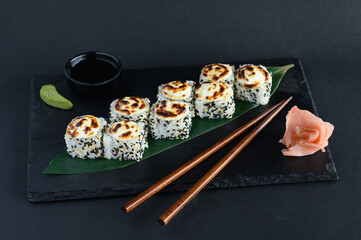 A set of sushi rolls on a wooden board and banana leaf, served with soy sauce, wasabi, ginger, and chopsticks. Perfect for an Asian restaurant menu.