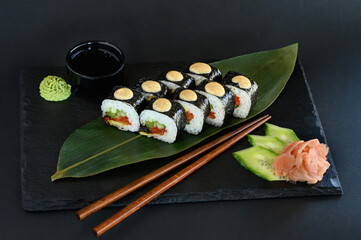 A set of sushi rolls on a wooden board and banana leaf, served with soy sauce, wasabi, ginger, and chopsticks. Perfect for an Asian restaurant menu.