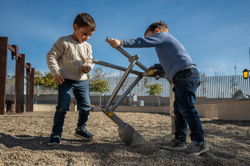 Two boys playing with a mechanical shovel in playground on sunny day