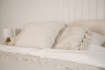 Beautiful light beige interior with soft white bed decorated with pillows in japandi and wawabi sabi style, cozy home concept