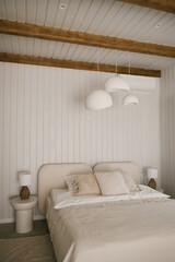 Beautiful light beige interior with soft white bed decorated with pillows in japandi and wawabi sabi style, cozy home concept
