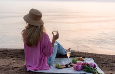 Summer picnic on the beach, bakery, fruits. Blond woman in hat. Rest time, sunset, nature