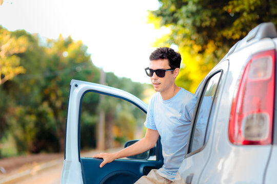 Casual traveler exiting a car during a scenic road trip. The man is dressed in light clothes, wearing sunglasses, with a natural and sunny outdoor background.