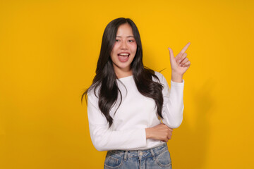 Young brunette woman pointing and showing something on yellow background