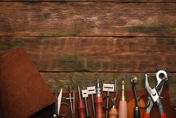 Leather and leatherworking tools on a leatherworker tanner workbench background.