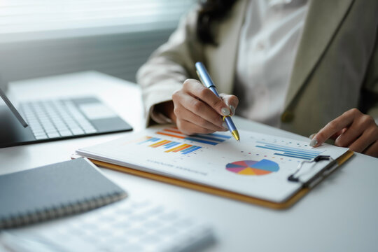 Businesswoman examining financial reports using pen, working with charts and graphs at office desk
