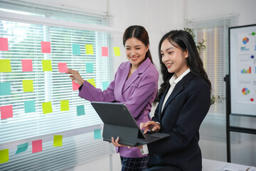 Two businesswomen are discussing over sticky notes in office using tablet