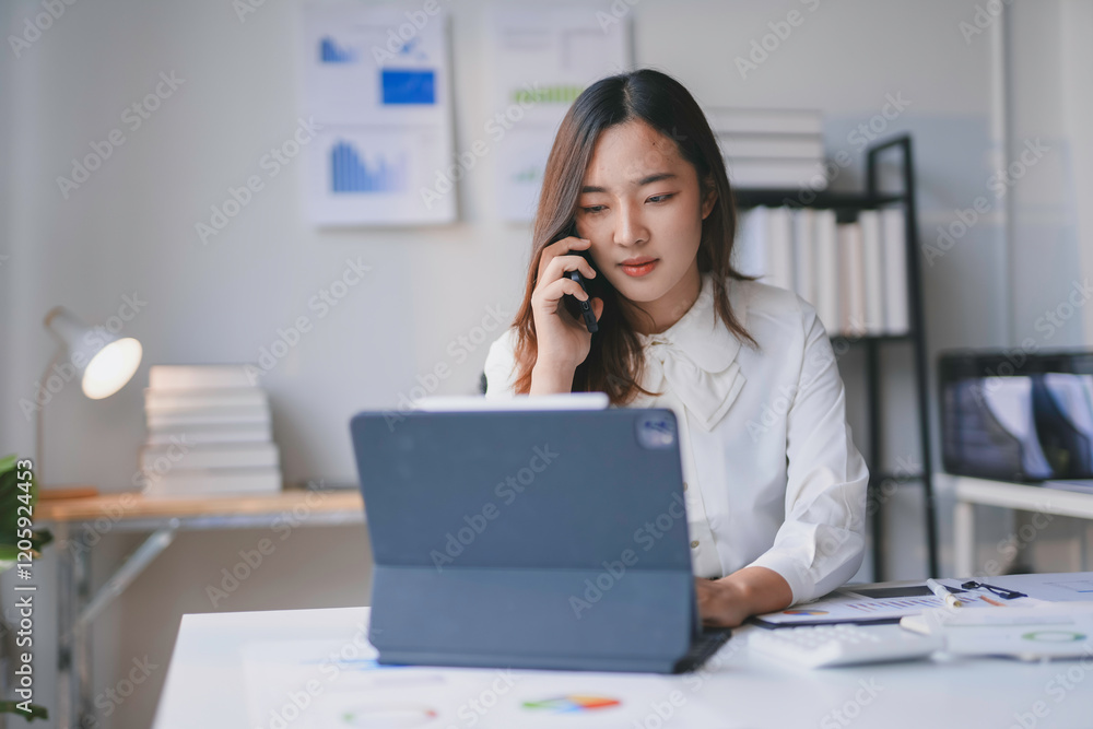 Poster young office worker using tablet and talking on mobile phone while working at desk