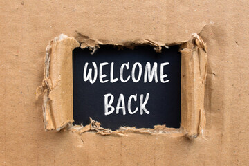 Welcome back message written on ripped torn cardboard paper with black background. Conceptual...