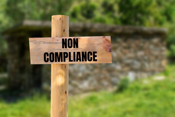 Non compliance message written on wooden sign with blurry nature background. Conceptual non compliance symbol. Copy space.