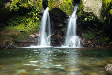 Fototapeta premium Moss-Covered Rocks Framing a Serene Waterfall