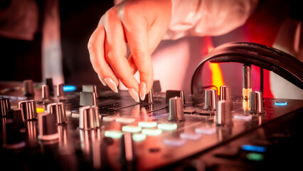 Close up DJ plays live set and mixing music on turntable console in the night club. Disc Jokey Hands on a sound mixer station at club party. DJ mixer controller panel for playing music and partying.